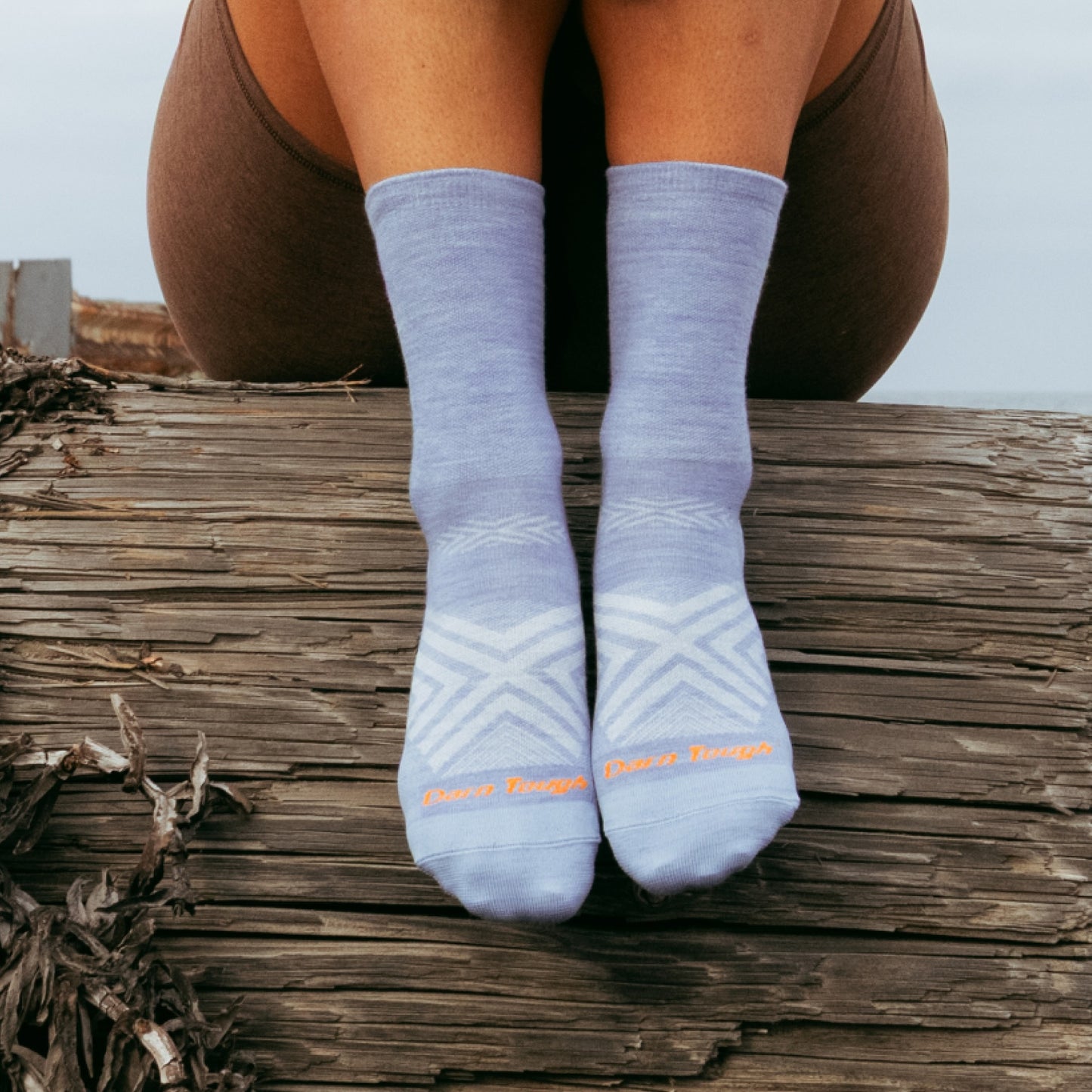 Person wearing light blue socks with a brand logo, sitting on wooden planks.