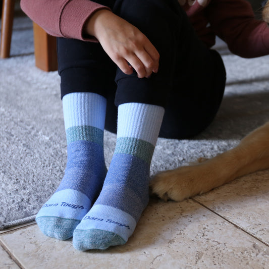 Person wearing blue striped socks sitting on a tiled floor with a dog's paw visible.