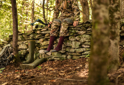 Darn Tough Women's over the calf hunting socks on model sitting on stone wall in woods