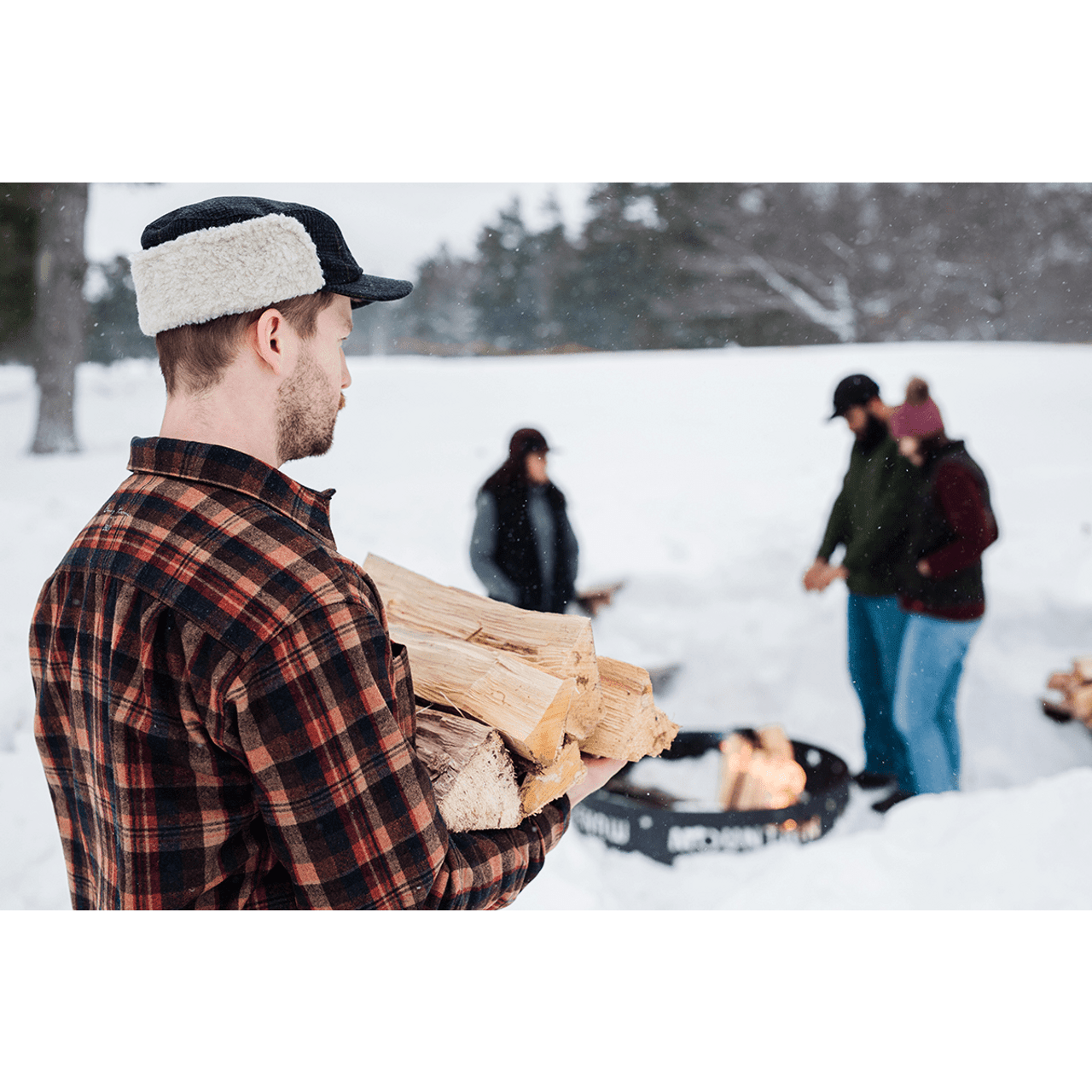 Model wearing Stormy Kromer Adirondack Plaid Bergland Cap outdoors carrying wood