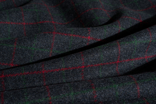 A close-up of dark charcoal gray wool fabric with a subtle woven texture, overlaid with a red and green windowpane plaid pattern.