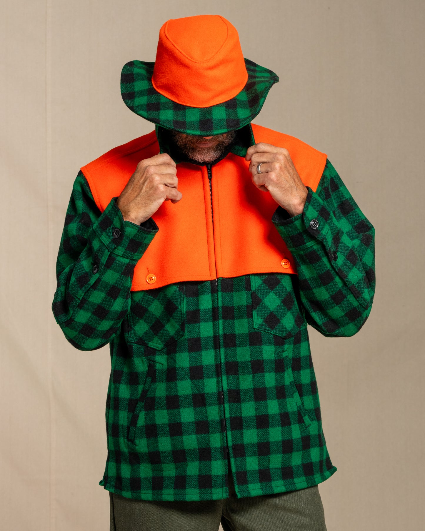Person wearing a green and black checkered wool jac shirt with an orange cape with a matching beagle crusher hat