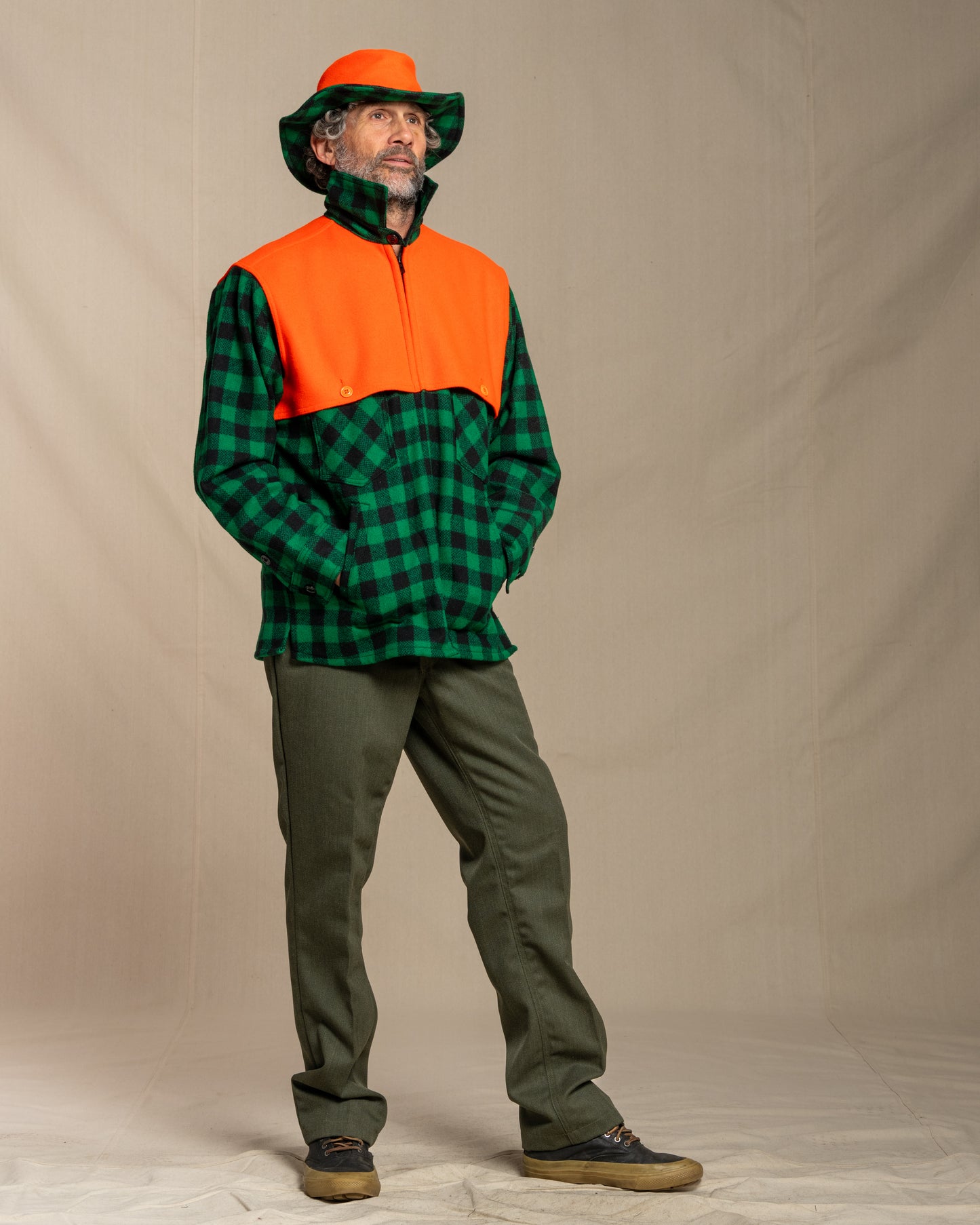 Person wearing a green and orange checkered wool jacket with a hat against a plain background