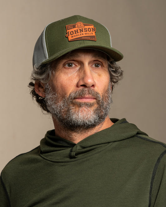 Man wearing a green cap and hoodie with a Johnson logo on a canvas background