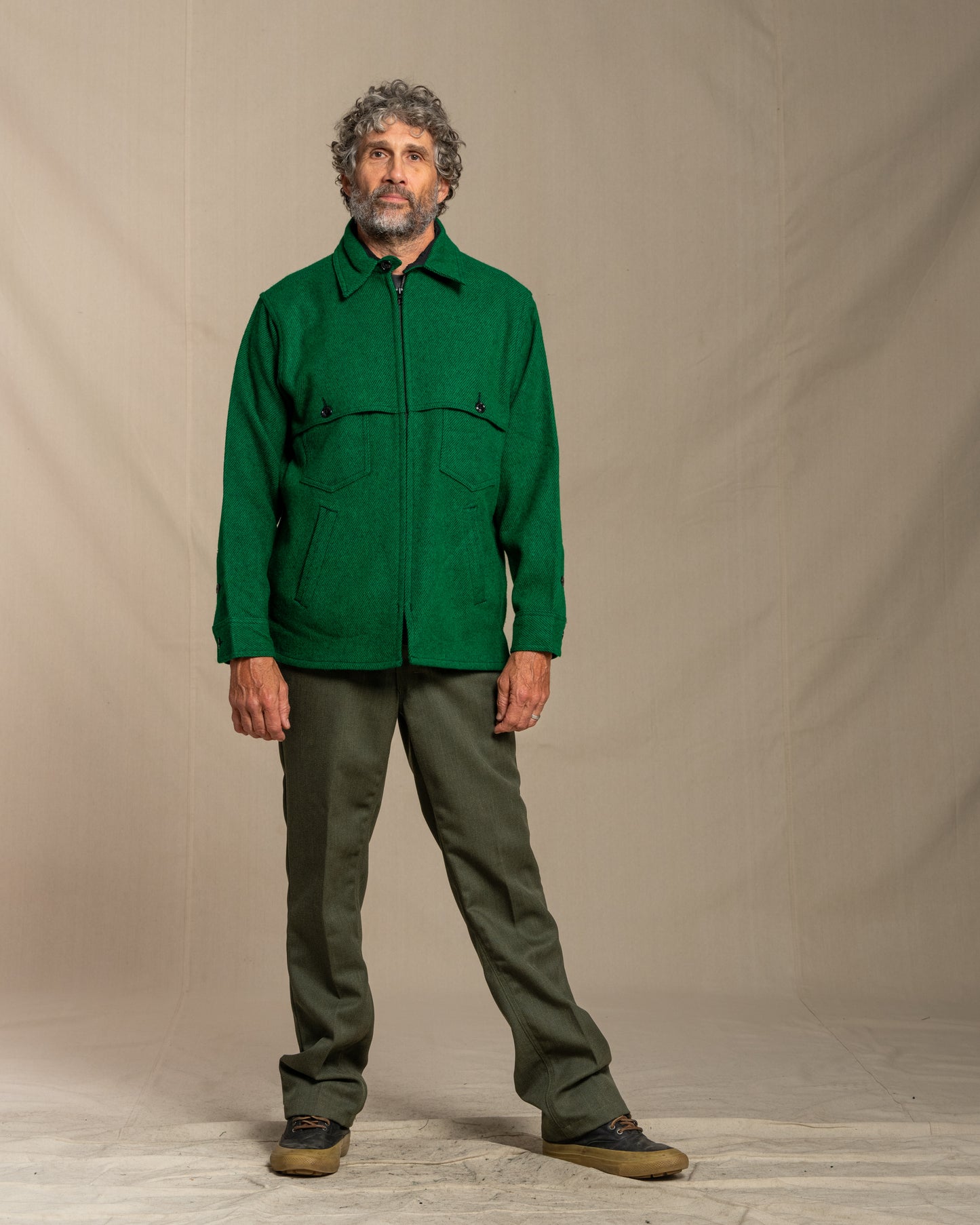 Man wearing a green twill wool jacket against a beige background