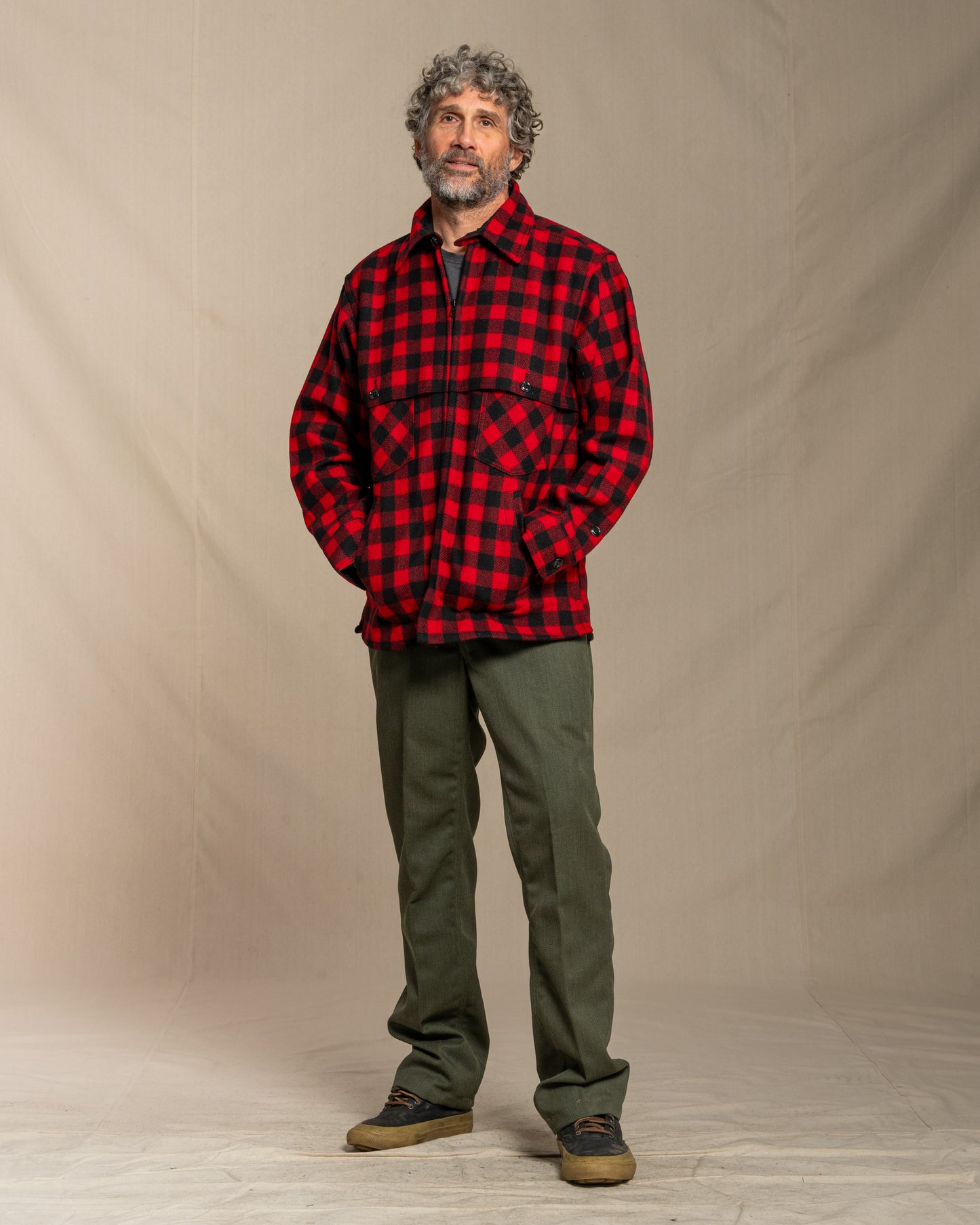Man wearing a red and black wool checkered jacket against a beige background