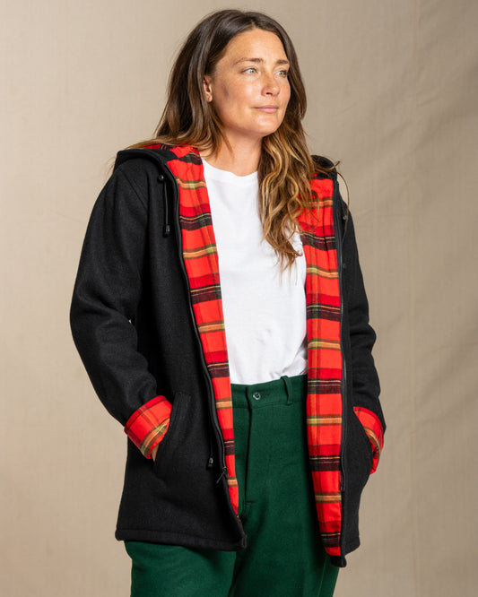 Person wearing a black wool coat with a red plaid hood against a beige background