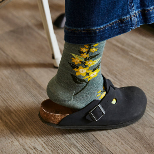 Person wearing a sock with floral design and a black shoe on a wooden floor.