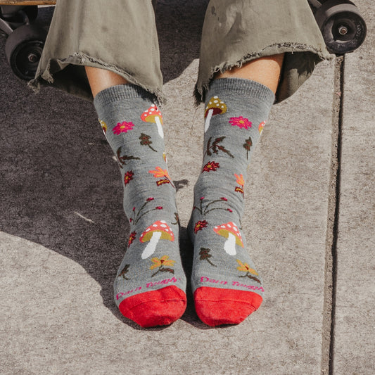 Person wearing gray socks with mushroom pattern and red toes on a sidewalk.