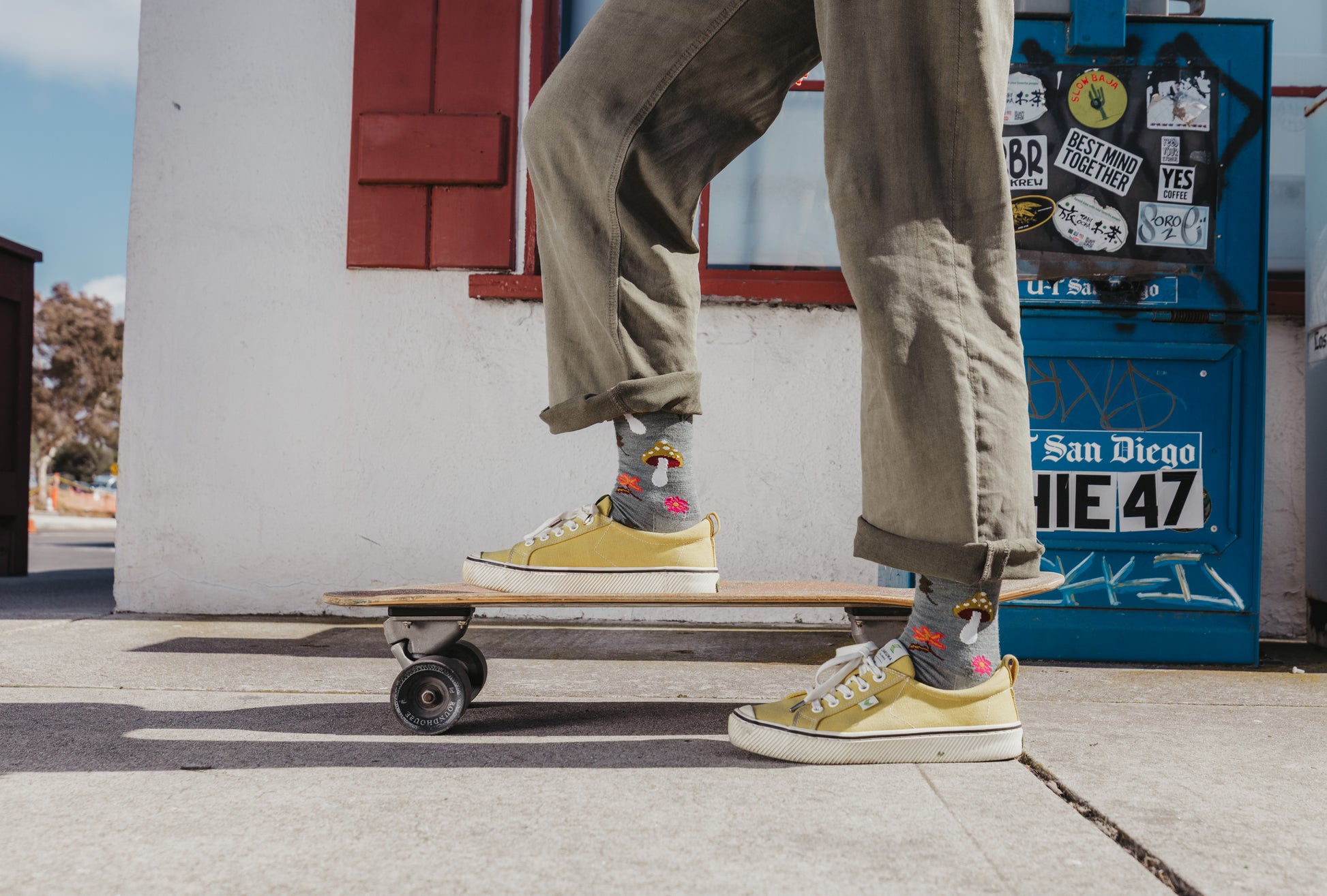 Person wearing yellow sneakers and colorful socks standing on a skateboard with a blue拒车 in the background.