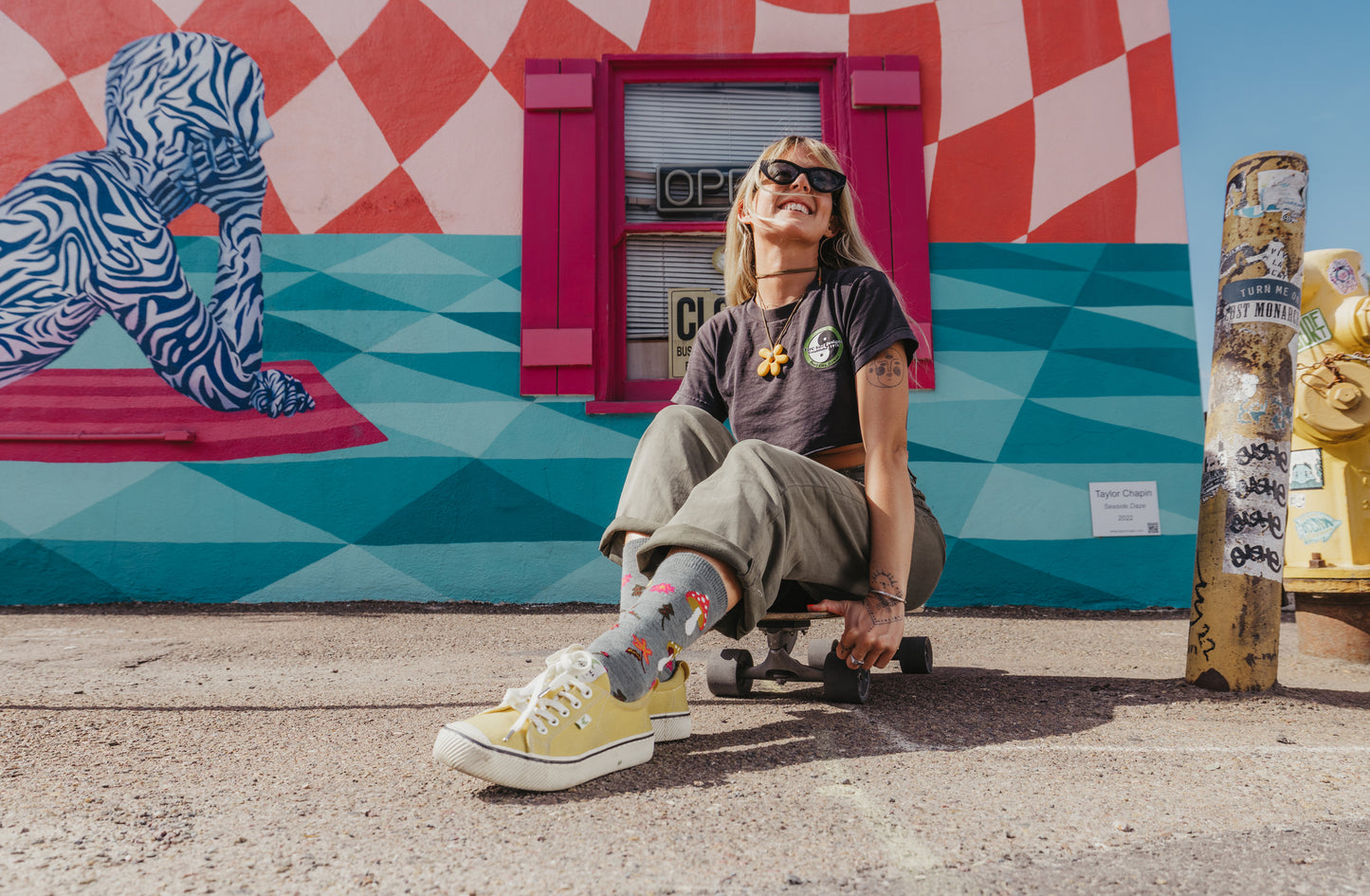 Person sitting on a skateboard in front of a colorful mural