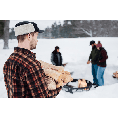 Model wearing Stormy Kromer Adirondack Plaid Bergland Cap outdoors carrying wood