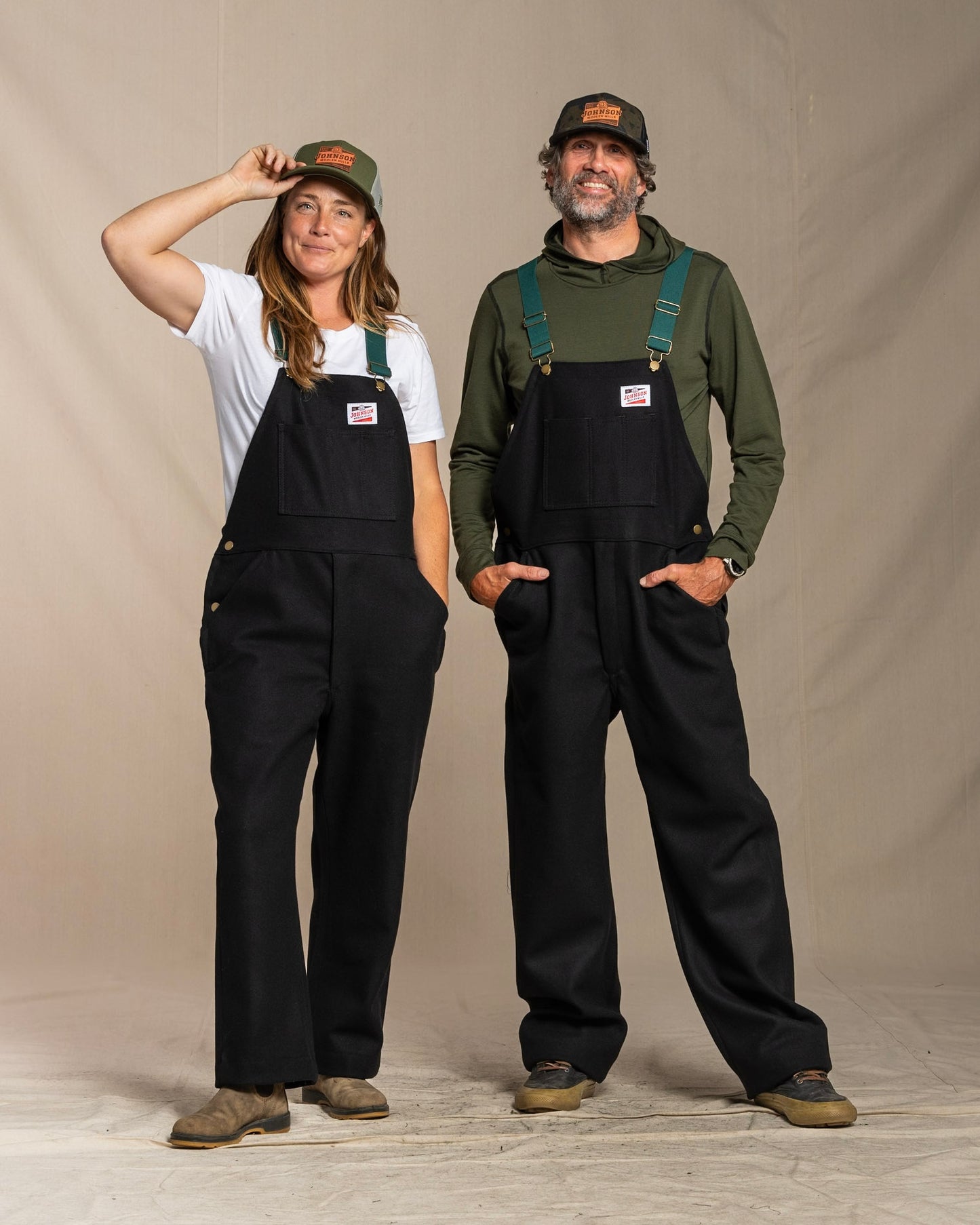 Two people wearing black wool overalls against a plain background