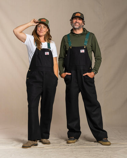 Two people wearing black wool overalls against a plain background