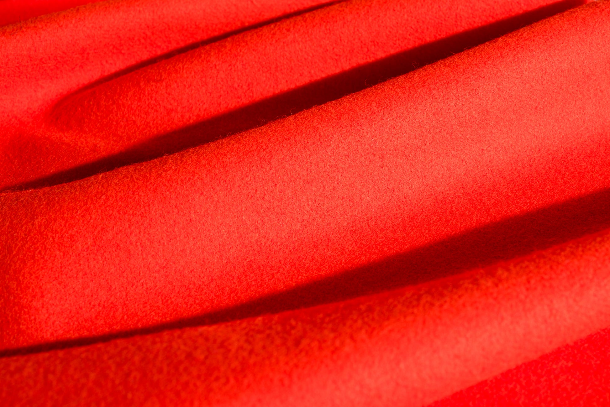 A close-up of a blaze orange wool fabric with a soft, textured weave and draped folds.