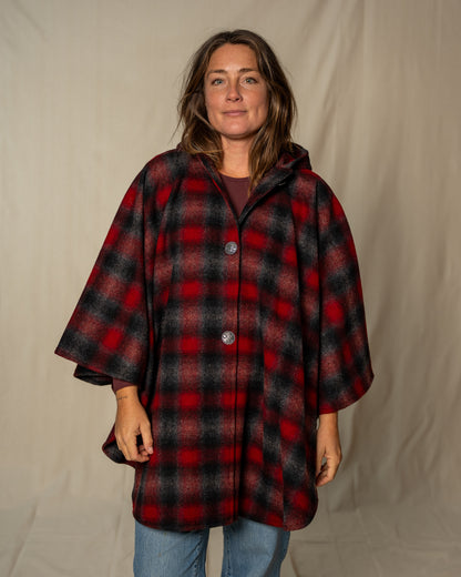 Woman wearing a red and black plaid poncho against a plain background
