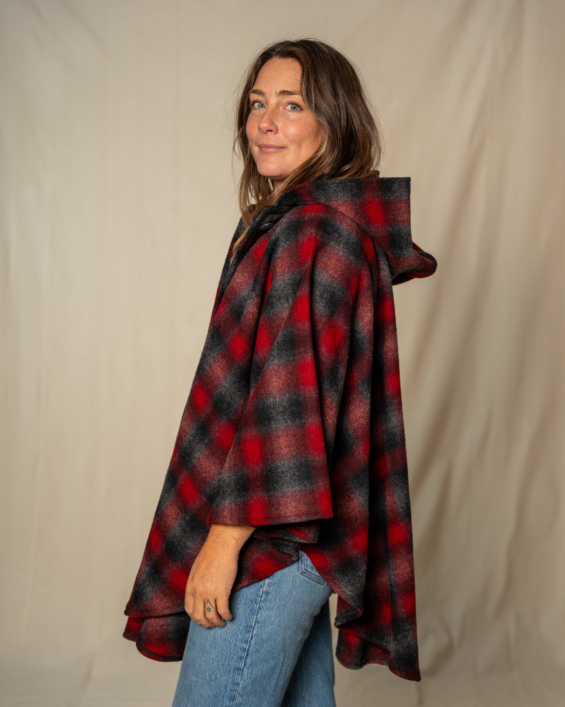 Woman wearing a red and black plaid poncho against a beige background