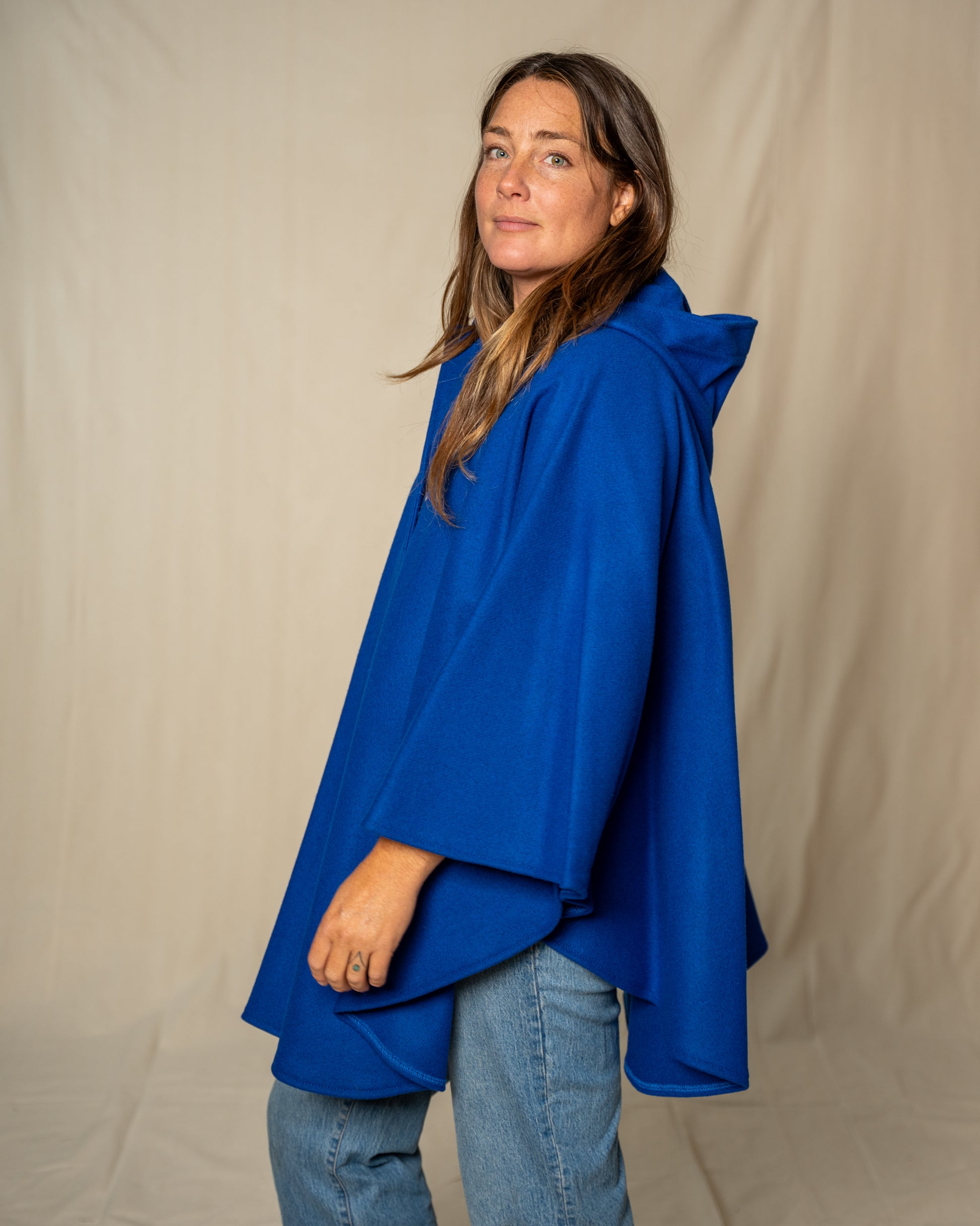 Woman wearing a blue hooded garment against a beige background