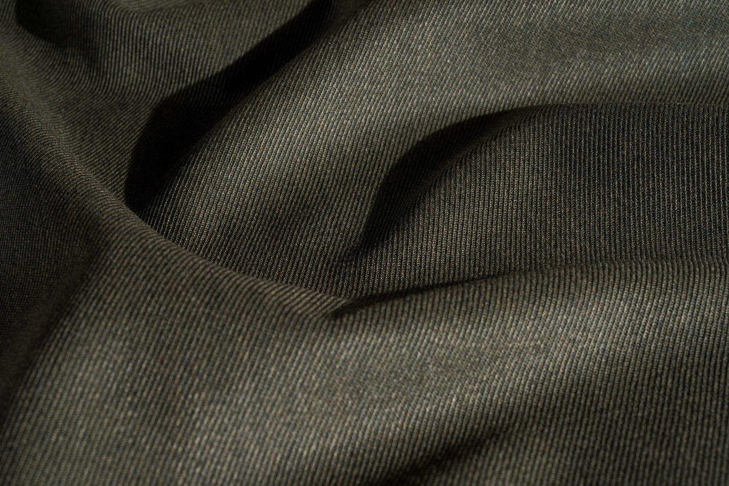 A close-up of a green wool worsted whipcord fabric with a soft, textured weave and draped folds.
