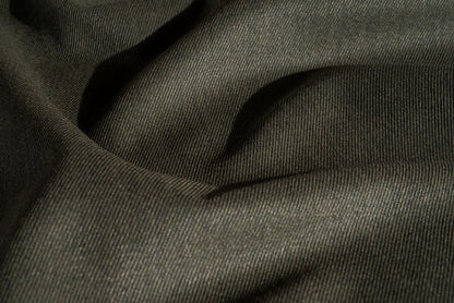 A close-up of a green wool worsted whipcord fabric with a soft, textured weave and draped folds.