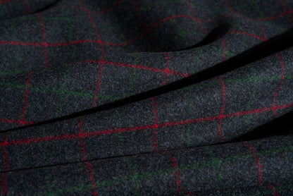 A close-up of dark charcoal gray wool fabric with a subtle woven texture, overlaid with a red and green windowpane plaid pattern.