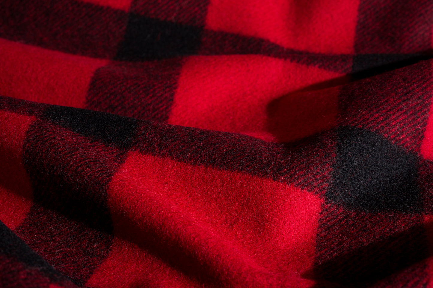 A close-up of red and black buffalo plaid wool fabric with a soft, textured weave and draped folds.