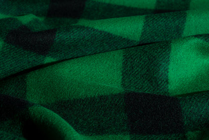 A close-up of green and black plaid wool fabric with a soft, textured weave and draped folds.