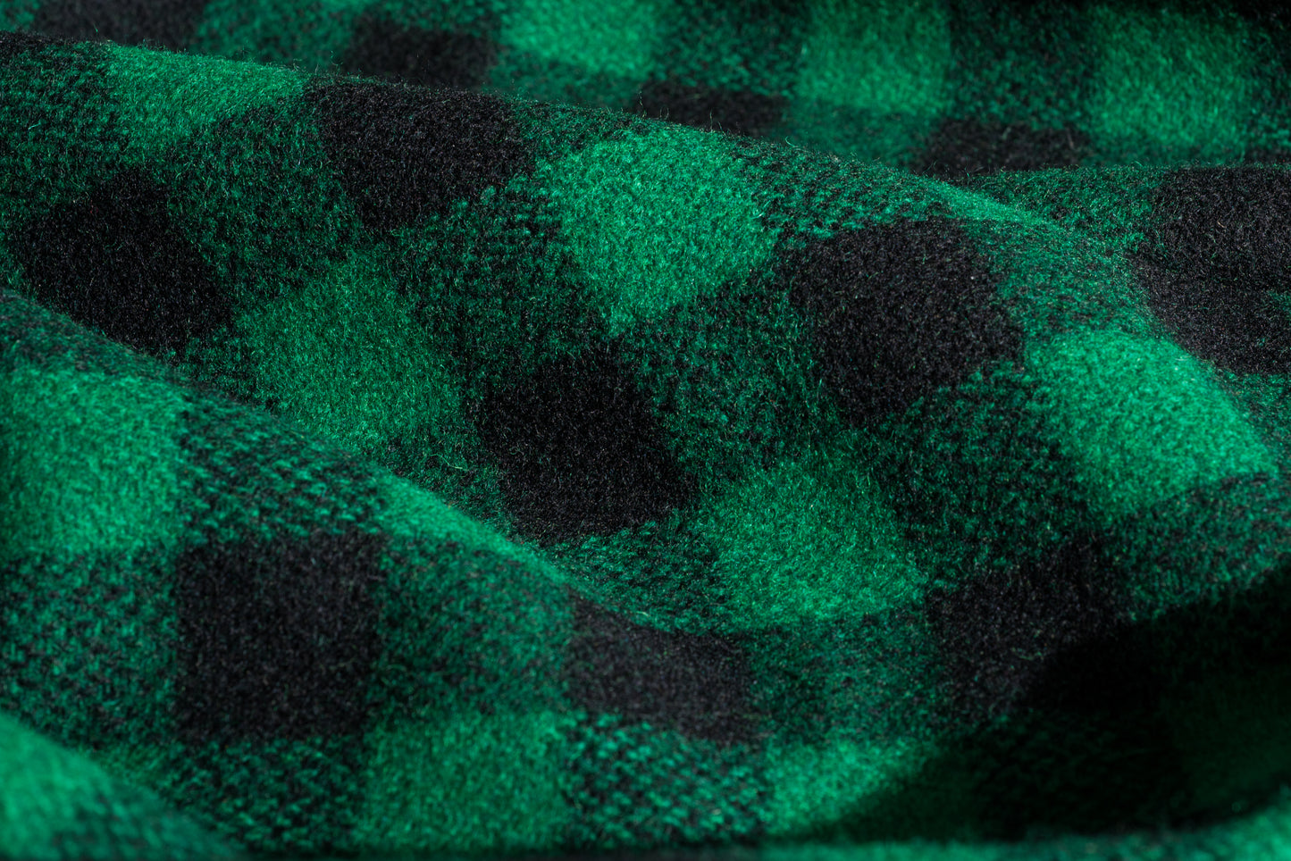 A close-up of a green and black buffalo plaid wool fabric with a soft, textured weave and draped folds.
