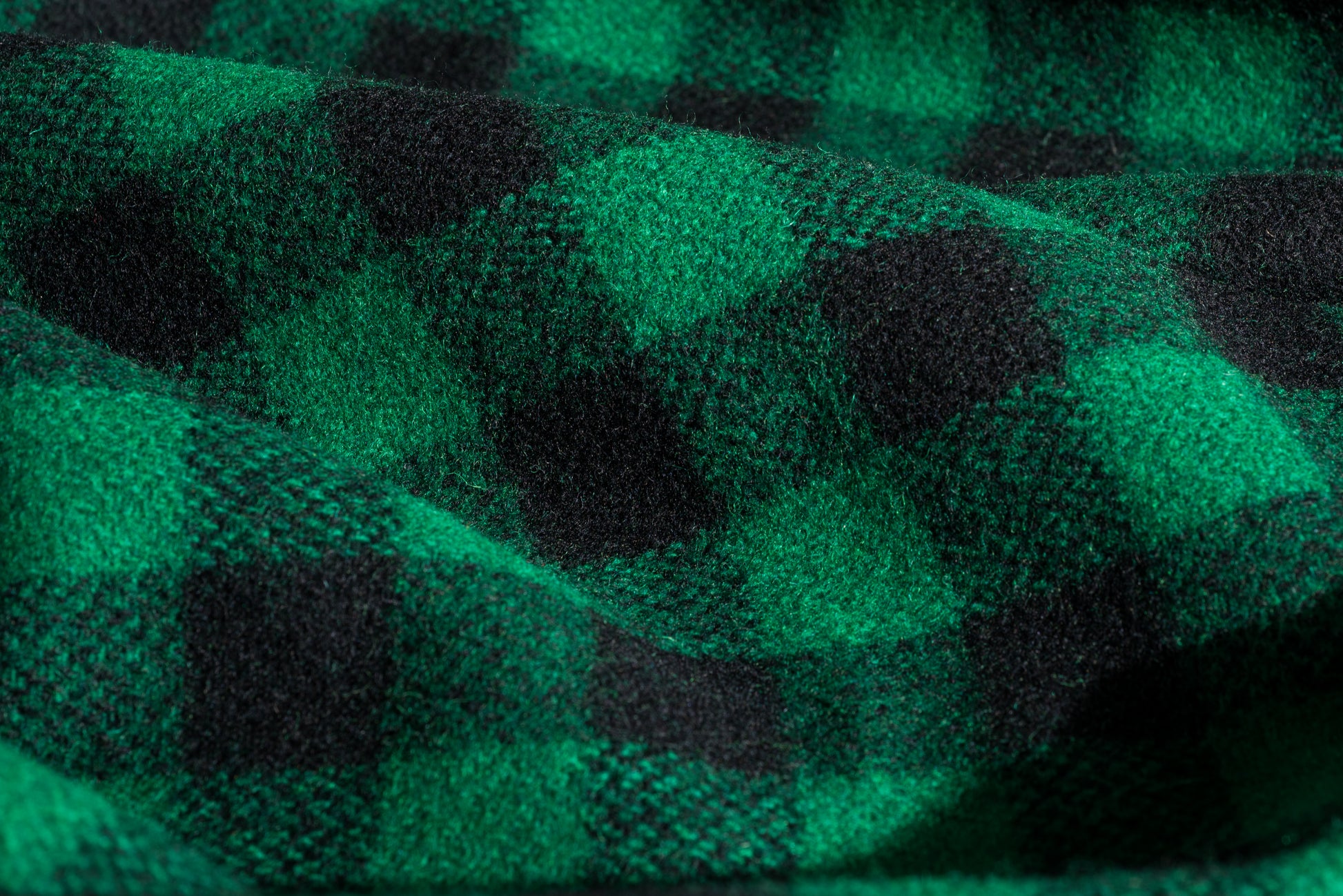 A close-up of a green and black buffalo plaid wool fabric with a soft, textured weave and draped folds.