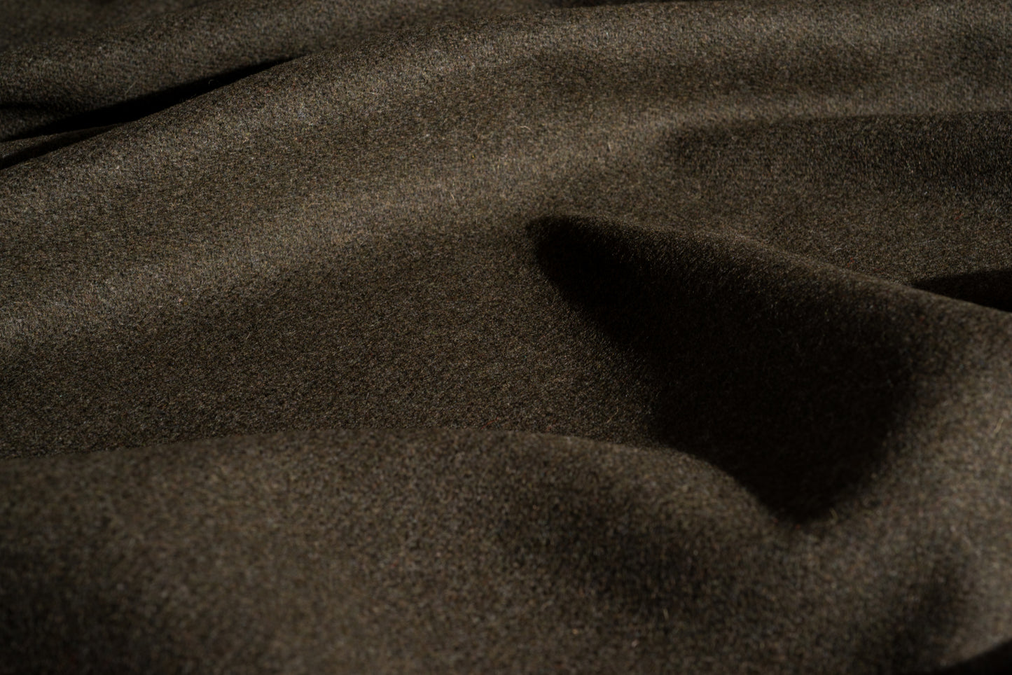A close-up of loden wool textured fabric with soft folds and shadows.