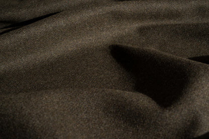 A close-up of loden wool textured fabric with soft folds and shadows.