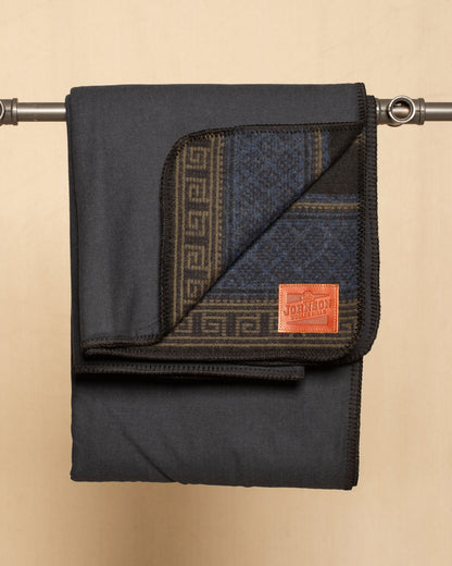 Folded flannel and wool blanket with geometric pattern and leather Johnson label on a beige background