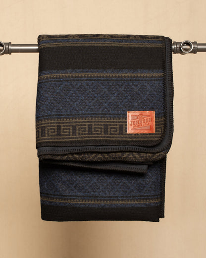 Folded flannel and wool blanket with geometric pattern and leather Johnson label on a beige background