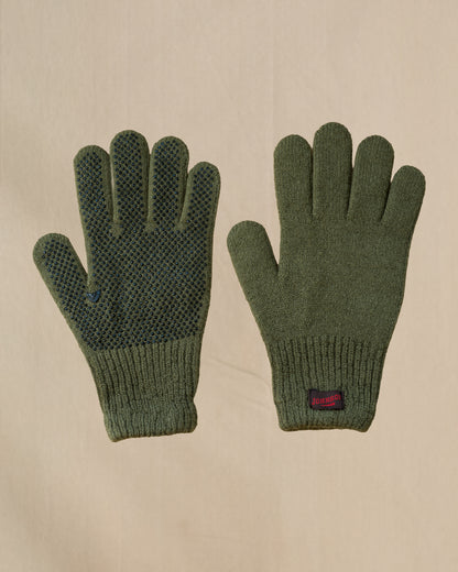 A pair of olive green merino wool knit gloves shown flat against a light beige background, with one glove displaying a textured grip pattern on the back of the hand and a small brown and red Johnson tab on the cuff.