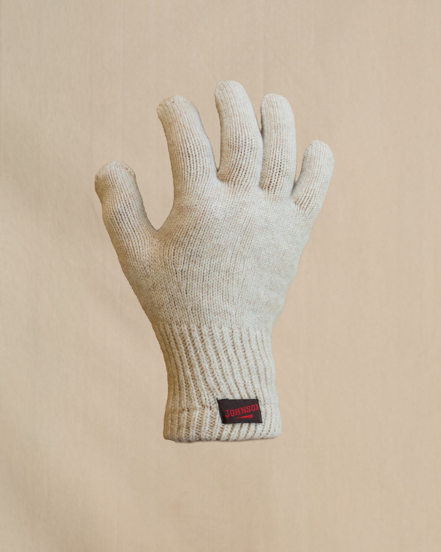 A single knit merino wool glove in light beige. The glove has a small brown and  red Johnson label on the cuff. 
