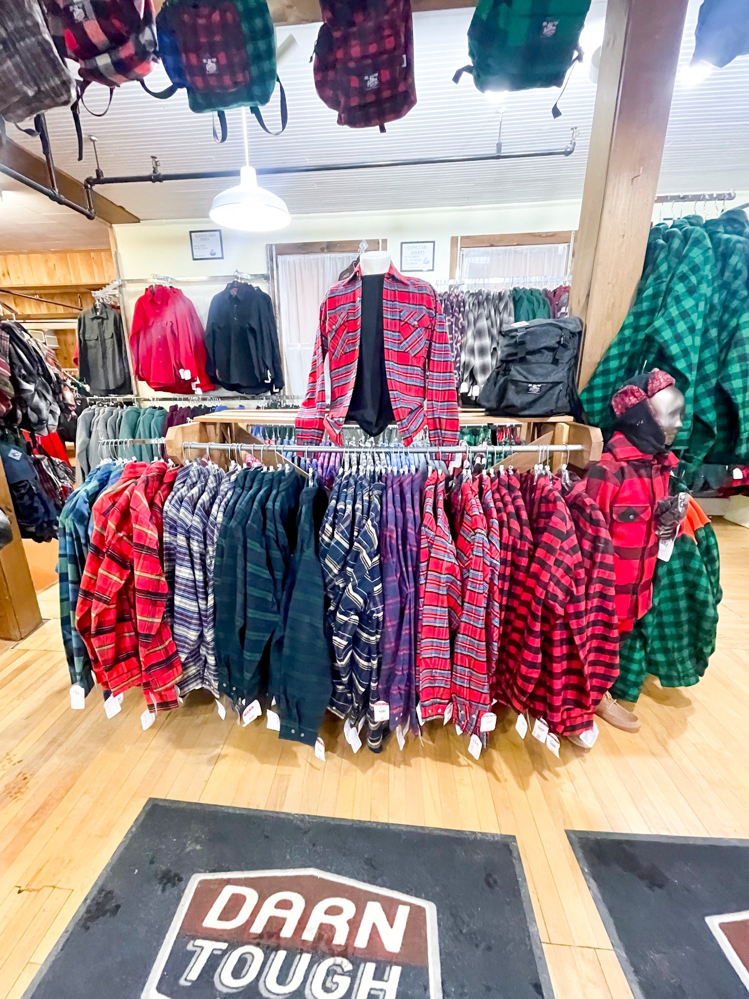 Store photo of various flannel shirts on rack, with darn tough floor mat