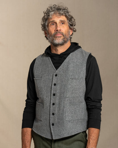 Man wearing a gray vest over a black shirt against a beige background