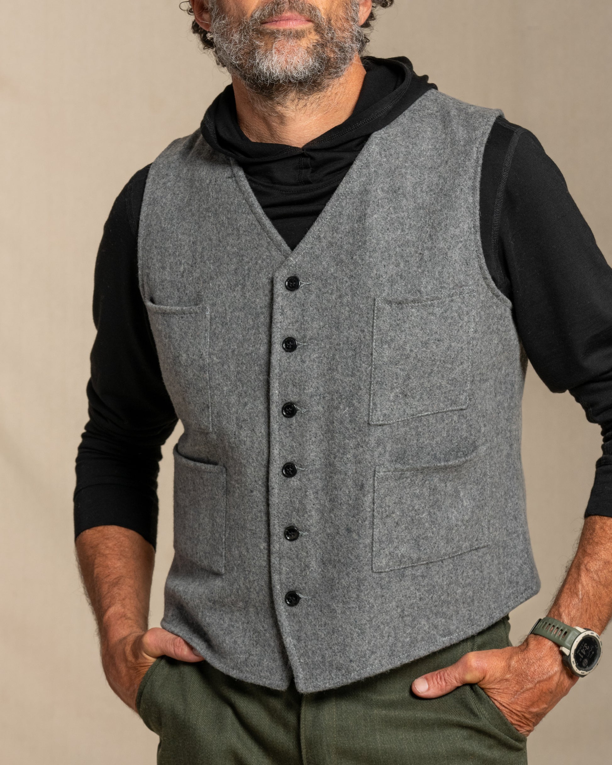 Man wearing a gray wool vest over a black shirt with a beige background