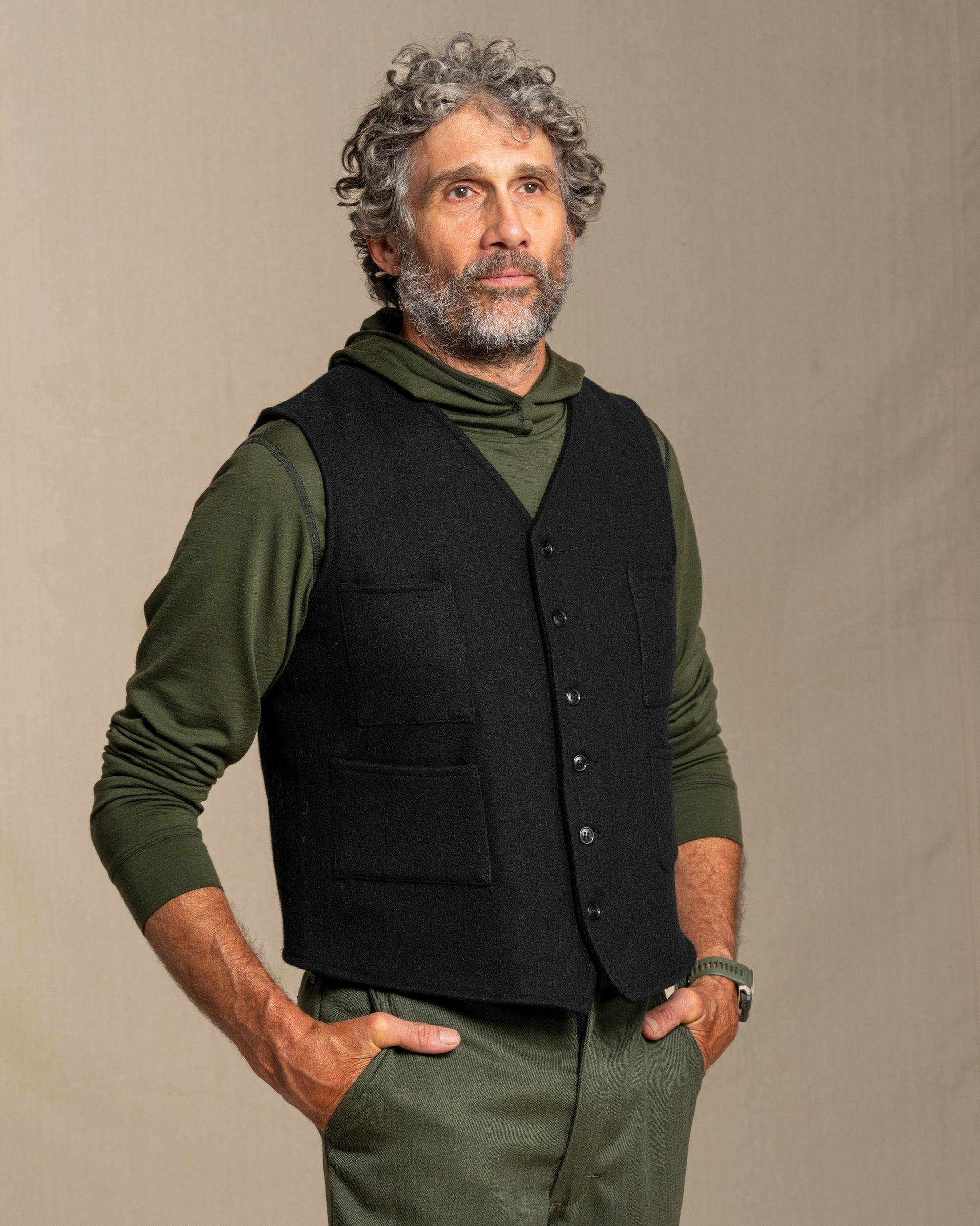 Man wearing a black vest over a green shirt with a neutral background