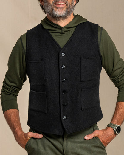 Man wearing a black wool vest over a green shirt with a neutral background