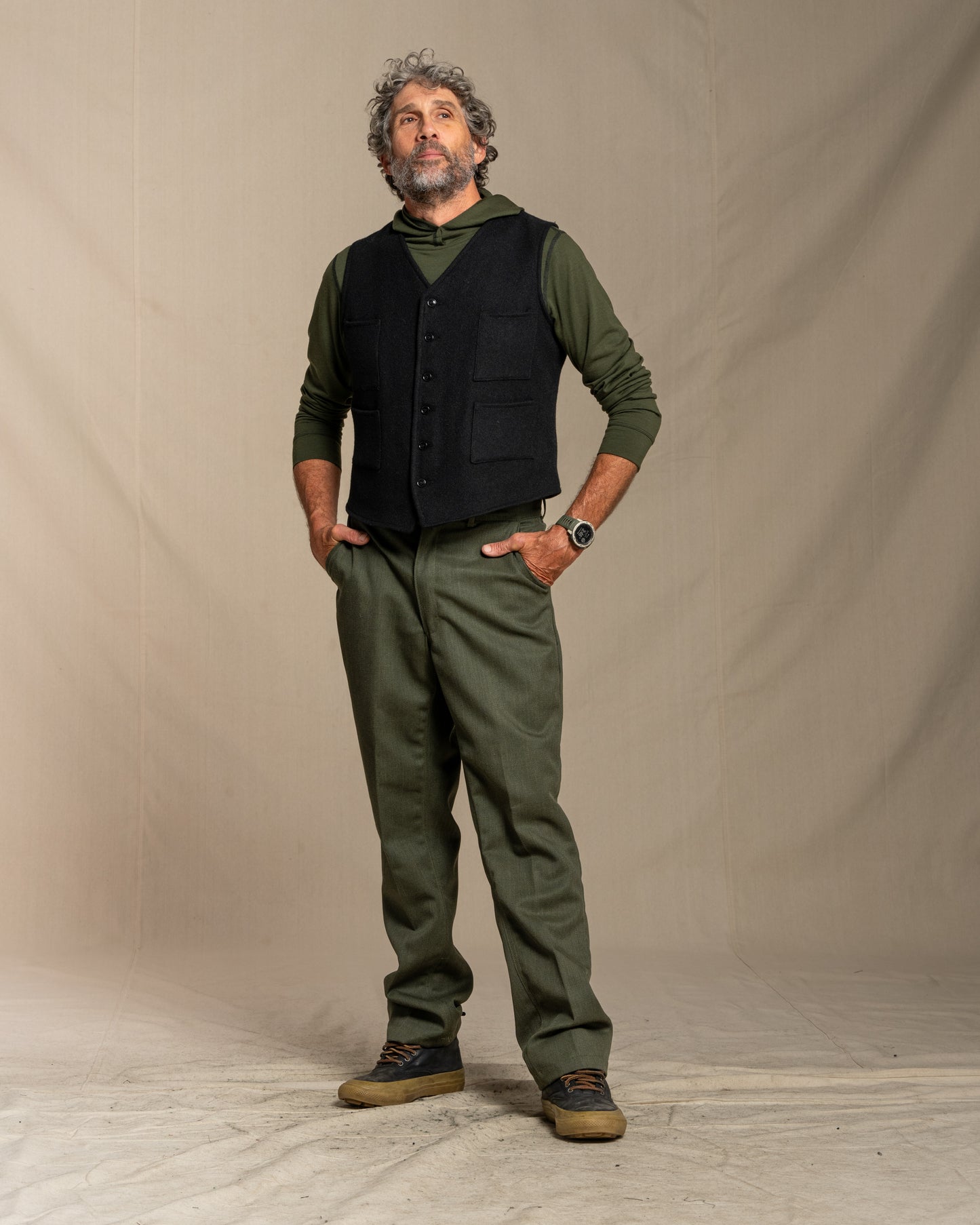 Man wearing a black vest over a green shirt with matching pants against a plain background