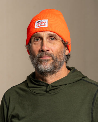Man wearing an orange beanie with Johnson logo against a beige background