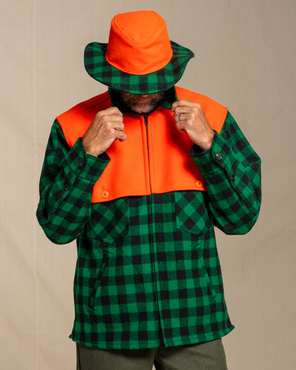 Person wearing a green and black checkered wool jac shirt with an orange cape with a matching beagle crusher hat