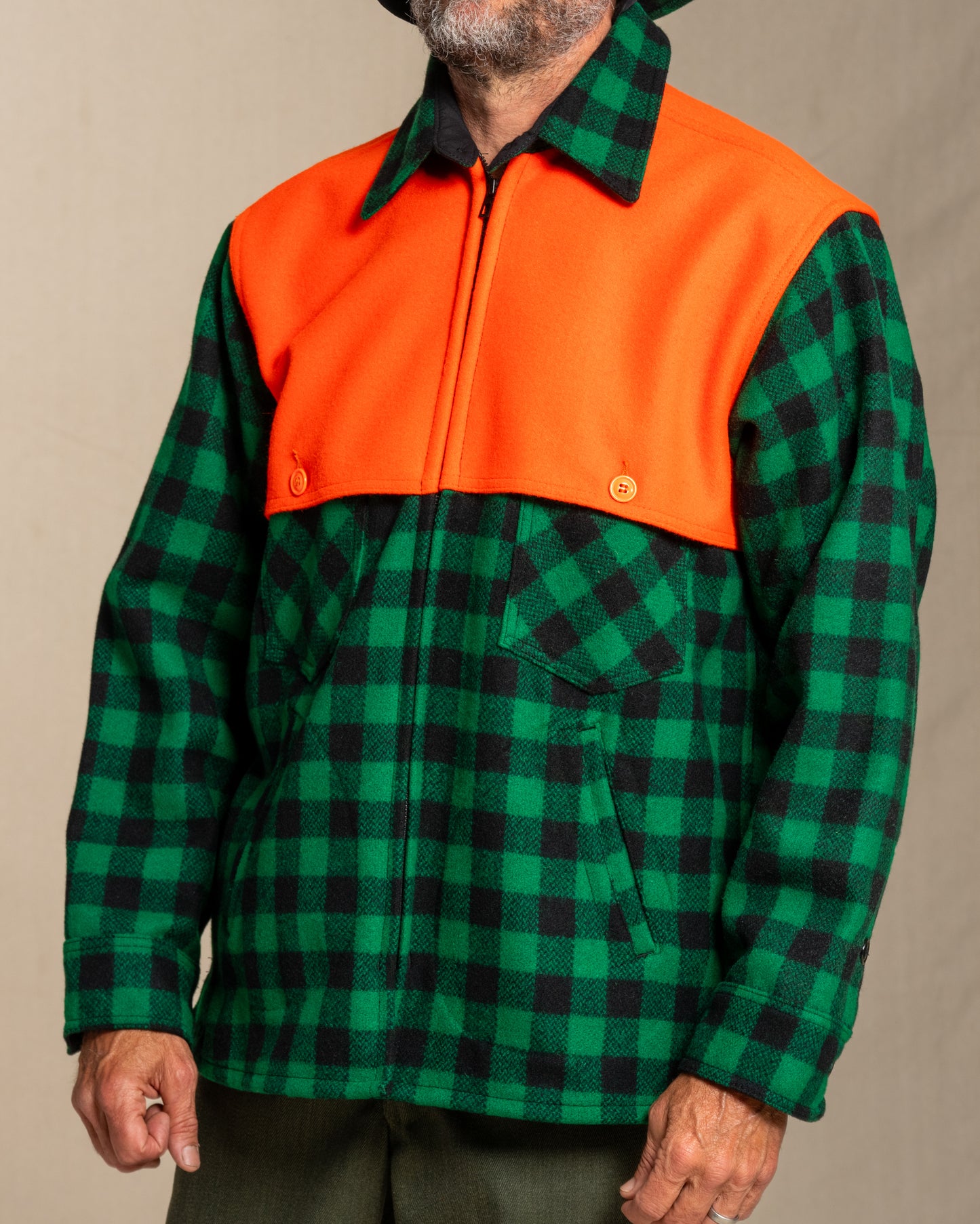 Person wearing a green and black checkered wool jacket with orange cape on a beige background