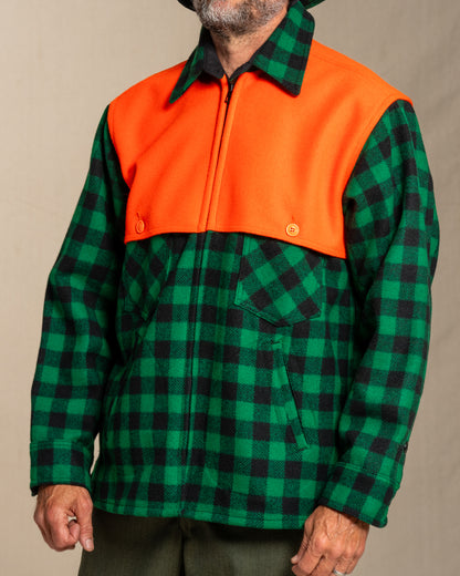 Person wearing a green and black checkered wool jacket with orange cape on a beige background