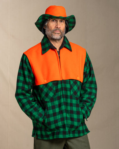 Person wearing a green and black checkered wool jac shirt with an orange cape with a matching beagle crusher hat