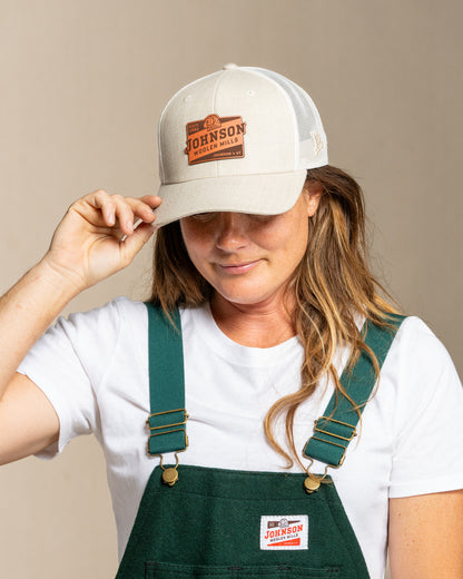 Person wearing a cap and green overalls with Johnson logo on a canvas background