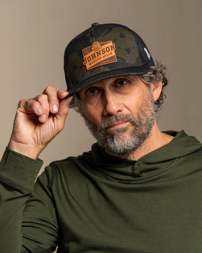 Man wearing a cap with a johnson logo against a neutral background