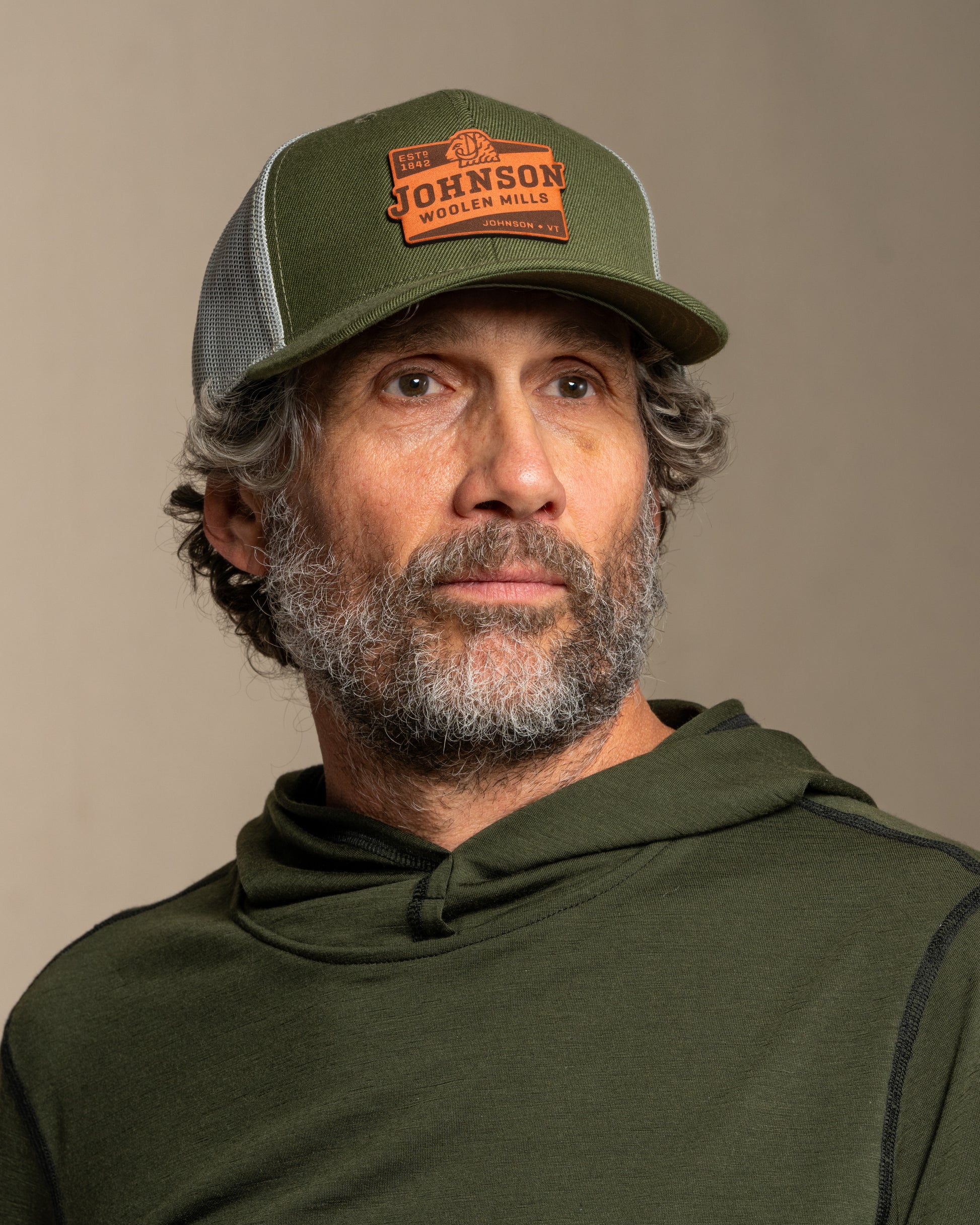 Man wearing a green cap and hoodie with a Johnson logo on a canvas background