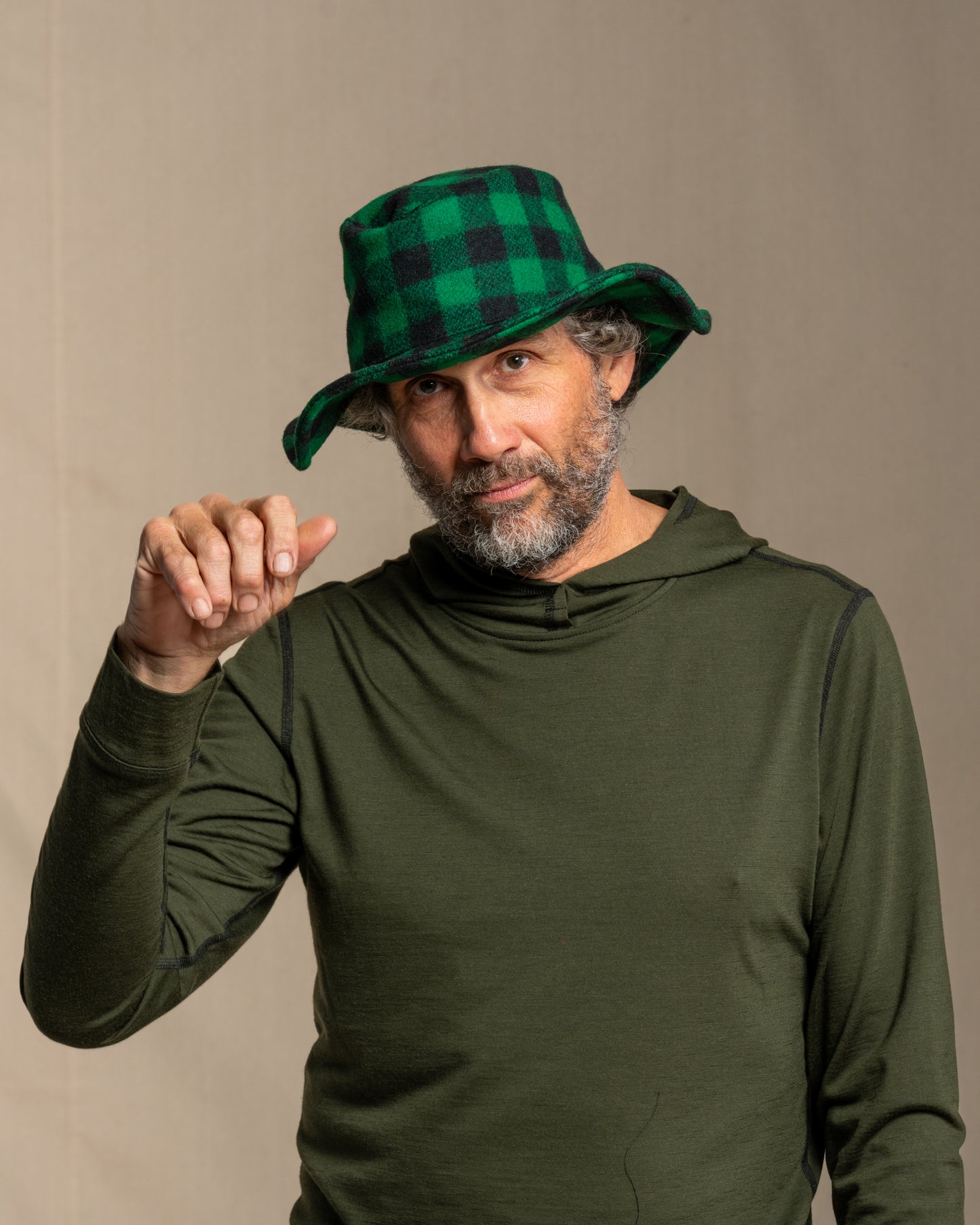 Man wearing a green plaid crusher hat and green merino wool hoodie against a canvas background